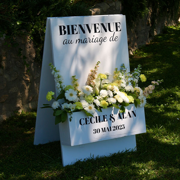 jardiniere de bienvenue au mariage avec lettrage noir et composition de fleurs jaune et vert