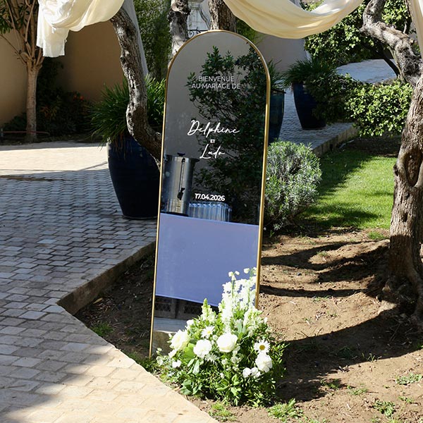 miroir avec lettrage blanc avec composition de fleurs au sol blanches et vertes avec voile de mariage