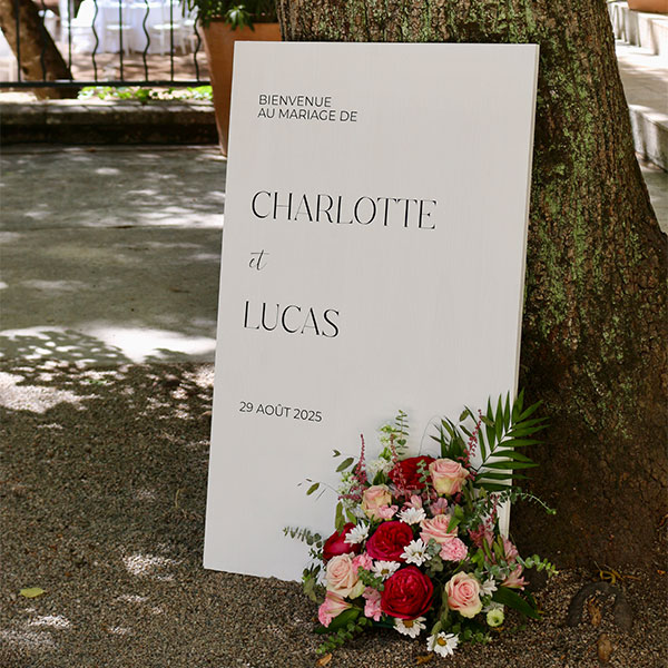 panneau de bienvenue blanc avec lettrage noir avec composition de fleurs rose au sol pour mariage